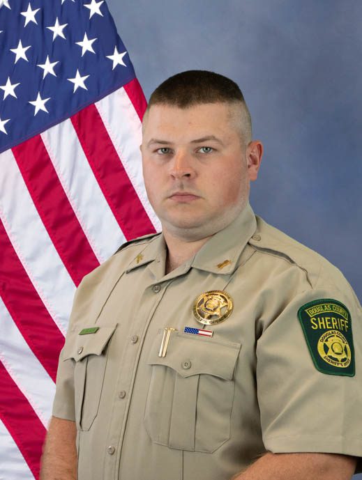 Portrait of a Douglas County sheriff's deputy in uniform standing in front of an American flag.