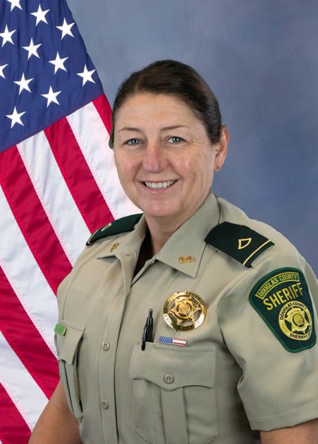 Portrait of a female sheriff's deputy in uniform with Douglas County Sheriff badge, standing in front of an American flag.