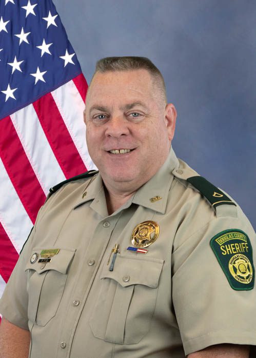 Portrait of a Douglas County Sheriff deputy in uniform standing in front of an American flag.