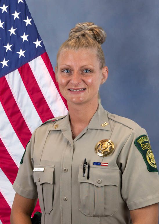 Portrait of a female sheriff officer in uniform with the American flag in the background, representing Douglas County Sheriff's Office.