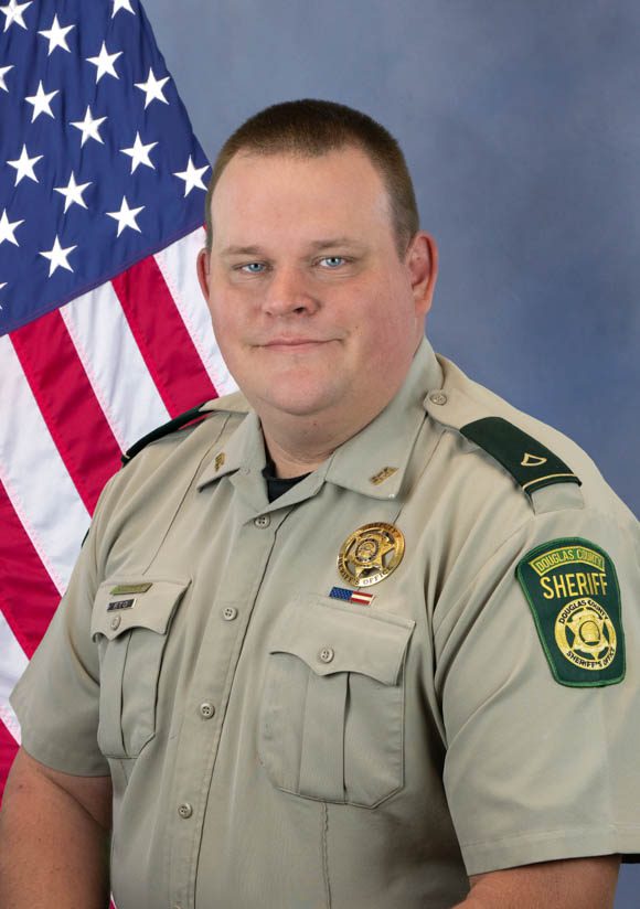 Portrait of a Douglas County Sheriff Department officer in uniform with badge and shoulder patch, posed in front of an American flag.