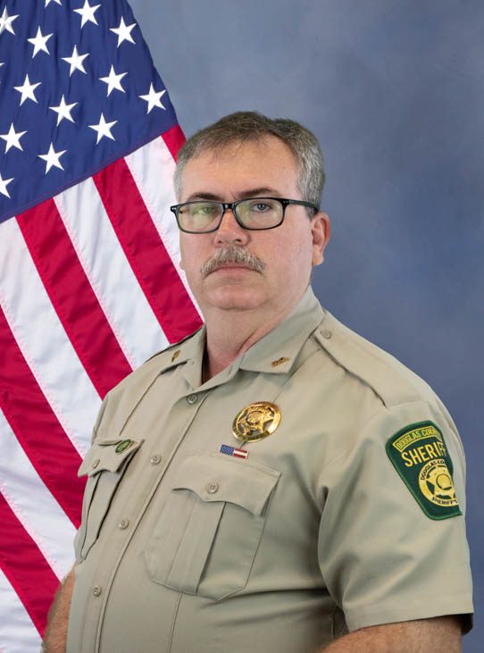 Portrait of a sheriff in uniform standing in front of an American flag.