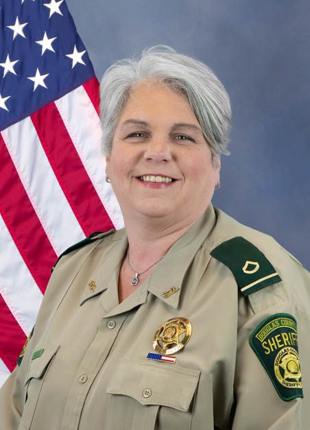 Portrait of a Douglas County Sheriff deputy in uniform standing in front of an American flag.